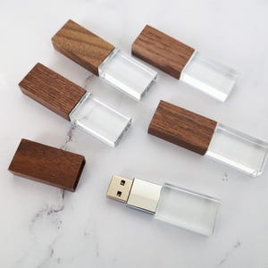 May include: Six wooden USB flash drives with clear plastic casings. The drives are arranged in a row on a white surface.