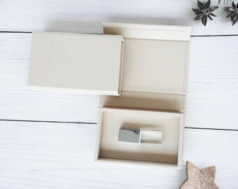 May include: A beige fabric box with a silver USB flash drive inside. The box has a hinged lid and a small compartment for the drive.