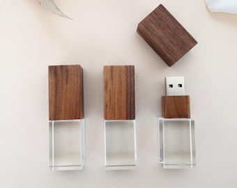 Puede incluir: Tres unidades flash USB con una base rectangular transparente y una parte superior de madera. Una unidad tiene el conector USB expuesto. Las partes superiores de madera son de color marrón cálido. Las unidades están dispuestas sobre una superficie clara.