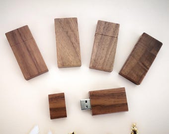 Puede incluir: Cinco unidades flash USB de madera en varios tamaños y formas. Las unidades están hechas de madera marrón oscura y tienen un acabado natural. Una unidad está conectada a una computadora.