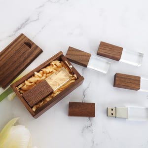 May include: A set of wooden USB flash drives with clear plastic casings. The drives are packaged in a wooden box with a lid. The box is filled with shredded paper.