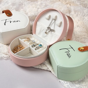 May include: Three round jewelry boxes with lids. The boxes are white, pink, and green. Each box has the name "Fran" written on the lid in black cursive. The pink box has a compartment for rings and earrings.