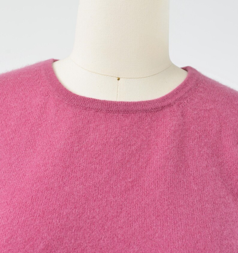 Neckline view of a vintage 1990s or Y2K pink cashmere sweater. Fitted, t-shirt style. Short sleeves. Crewneck. Displayed on a dress form with jeans.
