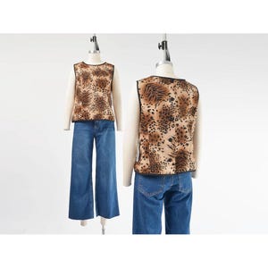 May include: A sleeveless top with a brown and black animal print, paired with blue denim wide-leg jeans. The top has a black trim around the neckline and armholes. The outfit is displayed on a mannequin against a white background.