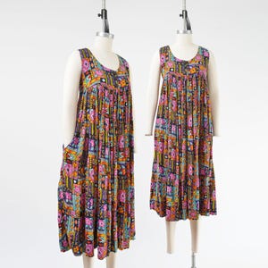 May include: Two sleeveless maxi dresses on mannequins. The dresses feature a colorful geometric pattern with pink, orange, blue, and yellow accents on a dark background. The dresses have a scoop neckline and a tiered skirt.