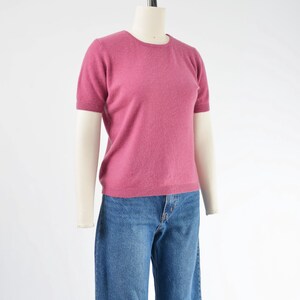 Side view of a vintage 1990s or Y2K pink cashmere sweater. Fitted, t-shirt style. Short sleeves. Crewneck. Displayed on a dress form with jeans.