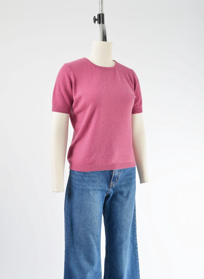 Side view of a vintage 1990s or Y2K pink cashmere sweater. Fitted, t-shirt style. Short sleeves. Crewneck. Displayed on a dress form with jeans.