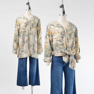 May include: Two vintage blouses and blue jeans are displayed on mannequins. The blouses have a V-neck and long sleeves, featuring a muted color palette with a floral and abstract pattern. One blouse is tied at the waist.
