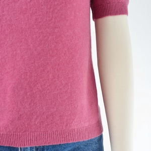 Hemline view of a vintage 1990s or Y2K pink cashmere sweater. Fitted, t-shirt style. Short sleeves. Crewneck. Displayed on a dress form with jeans.