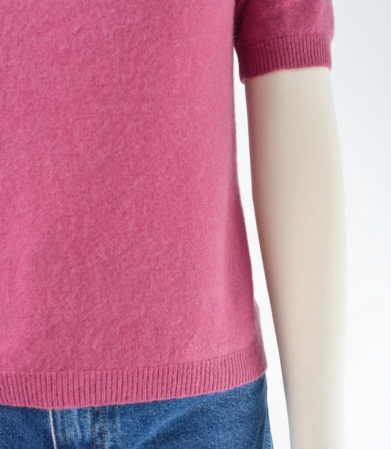 Hemline view of a vintage 1990s or Y2K pink cashmere sweater. Fitted, t-shirt style. Short sleeves. Crewneck. Displayed on a dress form with jeans.