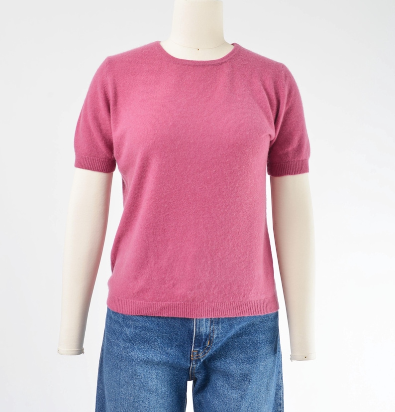 Front view of a vintage 1990s or Y2K pink cashmere sweater. Fitted, t-shirt style. Short sleeves. Crewneck. Displayed on a dress form with jeans.