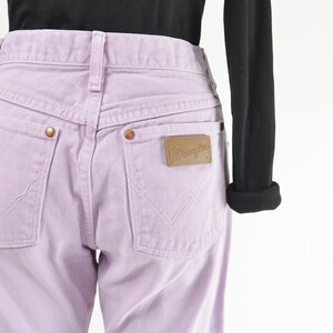 Vintage 90s western style Wrangler jeans. Light purple denim. High waisted. Straight legs. Displayed on dress form with a black t-shirt. Close up view of rear label on back pocket.