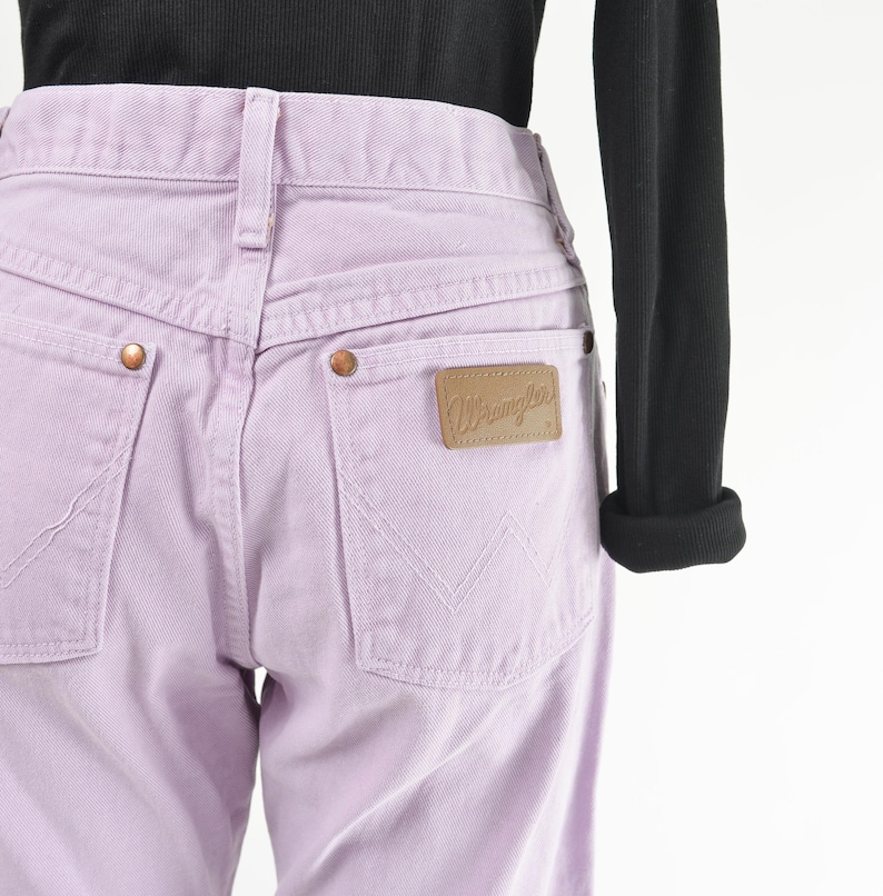 Vintage 90s western style Wrangler jeans. Light purple denim. High waisted. Straight legs. Displayed on dress form with a black t-shirt. Close up view of rear label on back pocket.