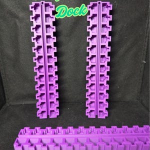 May include: Three purple plastic pieces for a 3D printer. The pieces are shaped like long rectangles with small squares along the sides. The text "PerfectPort Dock" is visible in the image.