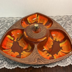 May include: A vintage serving dish with a triangular shape and a wood-grain design. The dish has three sections with orange and yellow accents, and a central lidded compartment. The lid has a gold-colored knob.