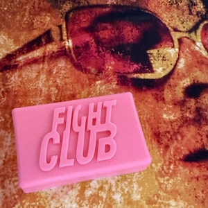 Könnte beinhalten: Ein rechteckiger, rosa Seifenblock mit den in Weiß geprägten Worten "FIGHT CLUB".
