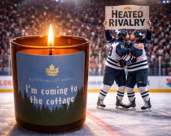 May include: A lit amber glass candle with a blue label that reads "Bold Soaps & Candles" and "I'm coming to the cottage." Two hockey players embrace, holding a sign that says "Heated Rivalry" in front of a crowd.