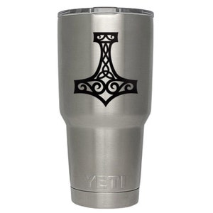 K&ouml;nnte beinhalten: Ein Edelstahlbecher mit geb&uuml;rsteter Metalloberfl&auml;che und transparentem Deckel. Auf der Vorderseite befindet sich eine schwarze Grafik eines Mjolnir-Hammers mit komplexen keltischen Knotenmustern. Der Markenname YETI ist am Boden eingepr&auml;gt.