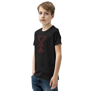 Pode incluir: Camiseta preta de manga curta com um s&iacute;mbolo de pentagrama vermelho na frente.
