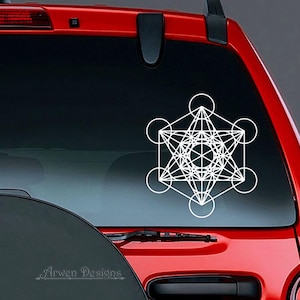 May include: White geometric design sticker on the rear window of a red car. The design is a complex, intricate pattern of lines and circles, resembling a sacred geometry symbol.