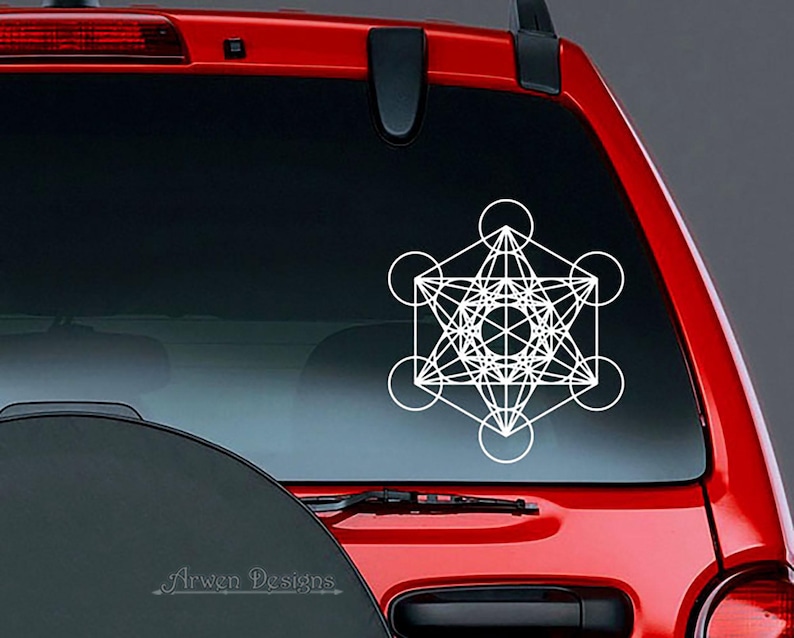 May include: White geometric design sticker on a red car's rear window. The design is a complex, intricate pattern of lines and circles, resembling a sacred geometry symbol.