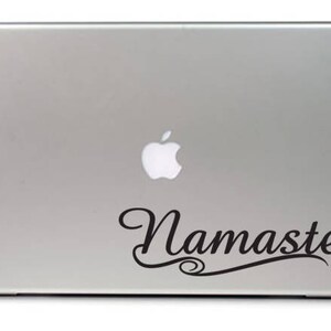 Puede incluir: Un port&aacute;til plateado con un logotipo de Apple negro y una pegatina de vinilo negro que dice "Namaste" en una fuente cursiva.