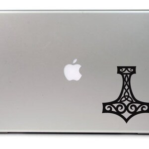 K&ouml;nnte beinhalten: Ein silberfarbener Laptop mit einem schwarzen Vinyl-Aufkleber auf dem Deckel. Der Aufkleber zeigt einen stilisierten Mjolnir, oder Thors Hammer, mit komplizierten Knoten- und Schn&ouml;rkelmustern, die in das Design des Hammers integriert sind.