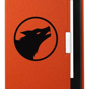 K&ouml;nnte beinhalten: Orangefarbene Kindle E-Reader-H&uuml;lle mit einer schwarzen Wolfssilhouette-Grafik in einem Kreis. Die H&uuml;lle hat eine strukturierte Oberfl&auml;che und ein Kindle-Logo an der Seite.