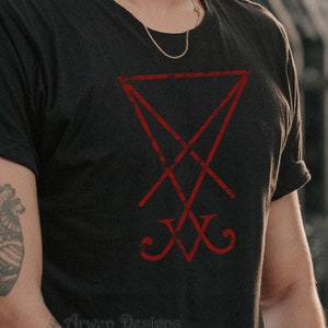 Pode incluir: Uma camiseta preta com um pentagrama invertido vermelho e desgastado. O texto "Arwen Designs" est&aacute; impresso na parte inferior da camiseta.