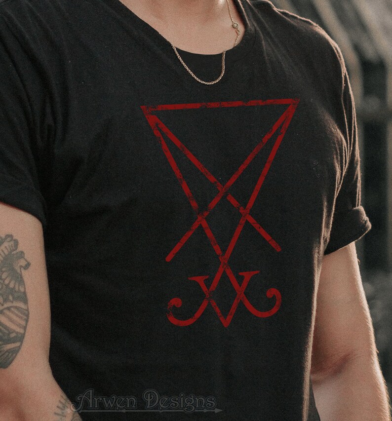 Pode incluir: Uma camiseta preta com um pentagrama invertido vermelho e desgastado. O texto "Arwen Designs" est&aacute; impresso na parte inferior da camiseta.