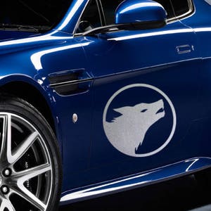 K&ouml;nnte beinhalten: Ein blaues Auto mit einem silbernen Wolfslogo an der Seite. Das Auto hat eine silberne Felge und eine schwarze Einfassung um die Fenster.