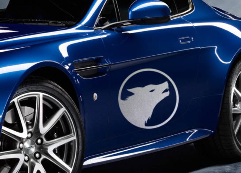 K&ouml;nnte beinhalten: Ein blaues Auto mit einem silbernen Wolfslogo an der Seite. Das Auto hat eine silberne Felge und eine schwarze Einfassung um die Fenster.