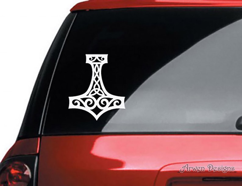 K&ouml;nnte beinhalten: Ein wei&szlig;er Vinyl-Aufkleber mit einem stilisierten Mjolnir-Hammer-Design und komplizierten keltischen Knotenmustern. Der Aufkleber ist auf der Heckscheibe eines roten Fahrzeugs angebracht. Der Text Arwen Designs ist unten rechts sichtbar.
