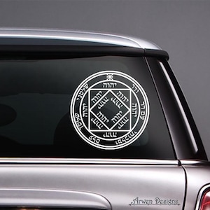 May include: White circular car decal featuring Hebrew text and geometric designs. The decal is applied to the rear window of a silver car. The text "Arwen Designs" is visible at the bottom.