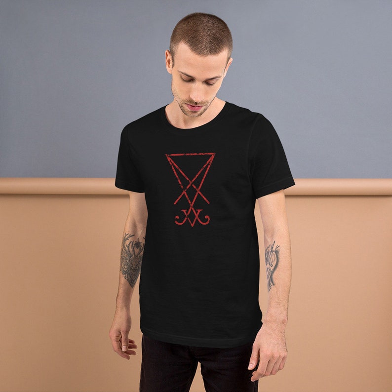 Pode incluir: Uma camiseta preta com um s&iacute;mbolo vermelho de pentagrama com uma cruz dentro. O s&iacute;mbolo &eacute; um s&iacute;mbolo comum associado ao satanismo.