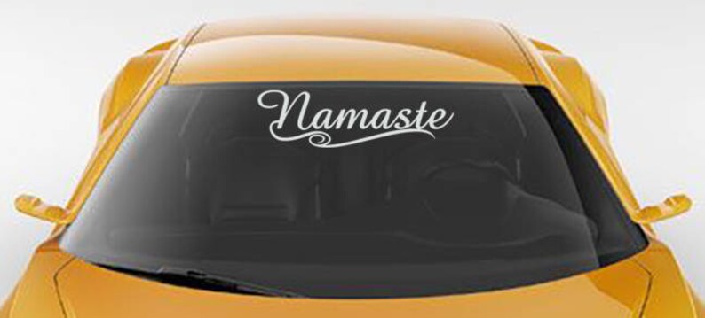 Puede incluir: Un coche amarillo con una calcoman&iacute;a de vinilo blanco en el parabrisas que dice "Namaste" en una fuente cursiva.