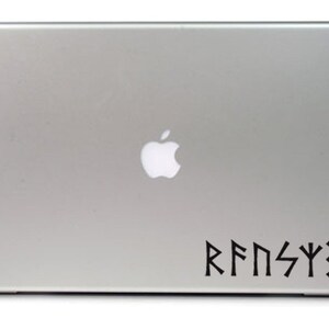 May include: A silver laptop computer with a black apple logo and a black vinyl sticker with the text "RFNSYX" in a stylized font.