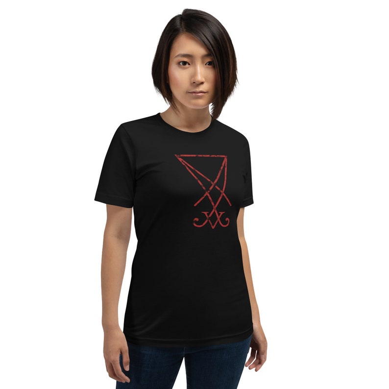 Pode incluir: Uma camiseta preta com um selo vermelho do Diabo estampado na frente.