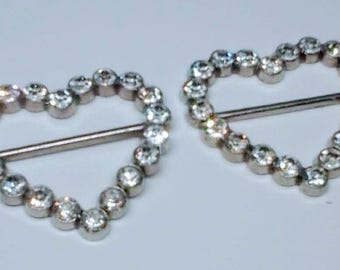 May include: Two heart-shaped silver-tone buckles, each outlined with clear, round rhinestones. A silver bar runs across the center of each heart. The buckles are set against a white background.