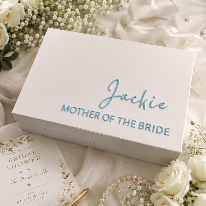 May include: A rectangular white gift box featuring the name Jackie in a light blue script font and the text MOTHER OF THE BRIDE in a light blue sans-serif font on the lid. The box has a smooth finish and a clean, minimalist design.