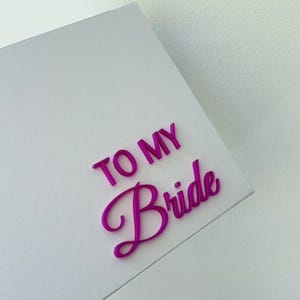 Puede incluir: Una caja rectangular blanca con el texto TO MY Bride en letras magenta vibrantes, brillantes y en relieve. Las palabras TO MY est&aacute;n en una fuente sans-serif negrita, mientras que la palabra Bride est&aacute; en una fuente cursiva elegante y fluida.