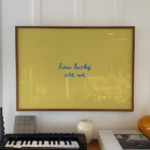 May include: A wooden console table displays a framed yellow artwork with the text "how lucky are we." A small black keyboard, a white vase, a stack of books, and an orange vase are also on the table.