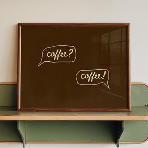 May include: A framed brown art print with the words "coffee?" and "coffee!" in white speech bubbles. The frame sits on a green and beige shelf attached to a white wall.