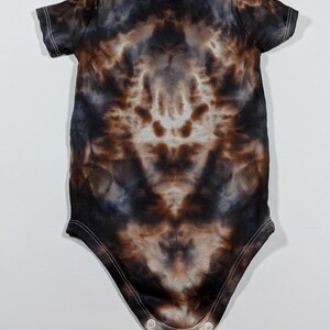 May include: A short-sleeved baby bodysuit with a tie-dye pattern in shades of brown, black, and blue. The bodysuit has a round neckline and snap closures at the bottom. The fabric appears soft and comfortable.
