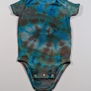 May include: A short-sleeved baby bodysuit with a tie-dye pattern in shades of blue, teal, and brown. The bodysuit has a round neckline and snaps at the bottom for easy changes. The fabric appears to be soft and comfortable.