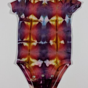 Puede incluir: Un body de beb&eacute; te&ntilde;ido con tinte en tonos morado, rojo y amarillo. El body de manga corta tiene un cierre de broches en la parte inferior y un cuello redondo. El patr&oacute;n colorido es sim&eacute;trico, con un dise&ntilde;o &uacute;nico.