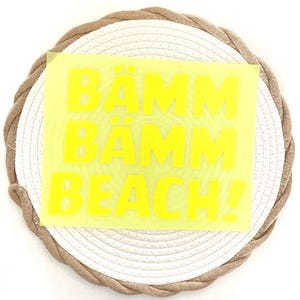 Könnte beinhalten: Ein leuchtend gelbes Quadrat mit den Worten "BÄMM BÄMM BEACH!" in fetten, gelben Buchstaben. Das Quadrat liegt auf einem weiß-beigen gewebten Untersetzer.