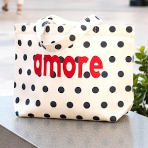May include: Cream-colored tote bag with black polka dots and the word "amore" in red. The bag has matching polka dot handles. A stylish and functional accessory for everyday use.