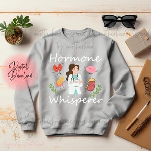 May include: A light gray sweatshirt with the words "Hormone Whisperer" and a graphic of a doctor and cartoon organs. The sweatshirt also has the words "Digital Download" in a pink circle.