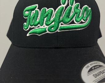 Puede incluir: Gorra snapback negra con el nombre "Tanjiro" bordado en verde con un contorno blanco. La gorra tiene una visera plana y un cierre a presión en la parte trasera. Estilo gorra de béisbol.